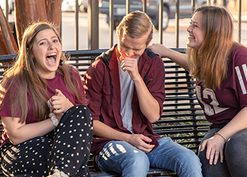 Three Aggie students sit on a park bench and laugh together.