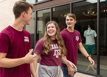 Three Aggie students walk along a sidewalk laughing together.